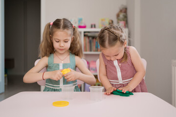 Obraz na płótnie Canvas Little girls with lovely faces play with clay molding shapes, learning through playing with colored plasticine developing creativity