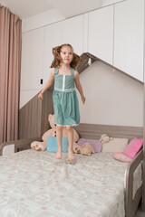 Obraz premium Happy funny little child girl in motion jumping on bed alone flying in air feeling joy, cheerful cute active kid having fun playing in bedroom