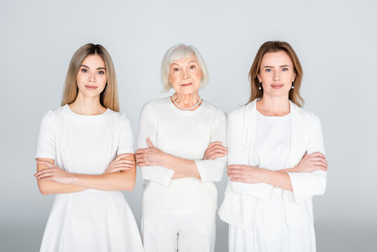three generation of women standing with crossed arms isolated on grey
