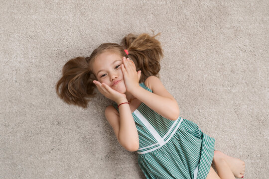 Cute preschool girl making funny faces, playing, having fun while lying on the soft carpet at home
