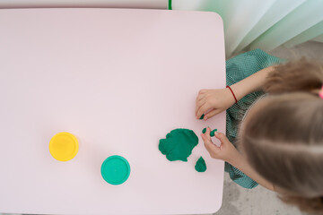 Little girl with a lovely face play with clay molding shapes, learning through playing with colored plasticine developing creativity
