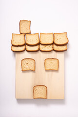 cottage made with rusks on wooden cutting board over white background