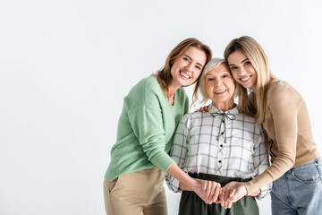 three generation of happy women looking at camera and holding hands isolated on white