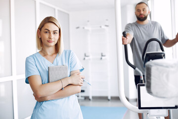 Obraz premium A woman is a physiotherapist. A man is using a spin bike. The patient is having a treatment.