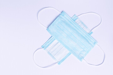 Two cross shaped disposable medical masks on a white background with empty space. Stop the spread of the coronavirus.