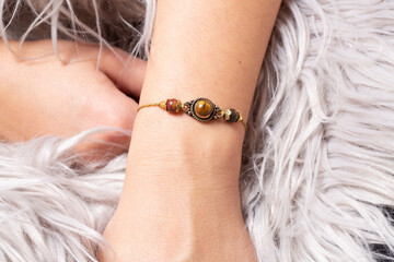 Female hand wrist wearing brass golden bracelet with tyger eye mineral stone