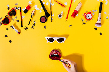 Stylish composition of cosmetics, sunglasses, red shiny brooches on orange background