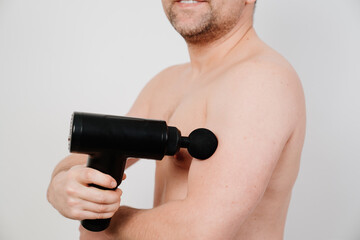 Fototapeta na wymiar man uses massage gun. medical-sports device helps to reduce muscle pain after training, helps to relieve fatigue, affects problem areas of body, improves condition of skin.