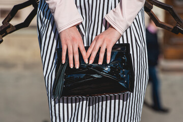 Fashionable woman in striped dress hold big black handbag. Street style city wall background