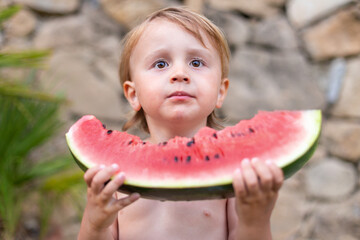 Child eating watermelon in the garden during summer vacances. Kids eat fruit outdoors. Healthy snack for children. Little boy tasting a slice of water melon.