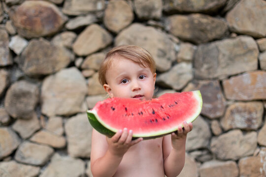 Child eating watermelon in the garden during summer vacances. Kids eat fruit outdoors. Healthy snack for children. Little bpy playing in the garden holding a slice of water melon.