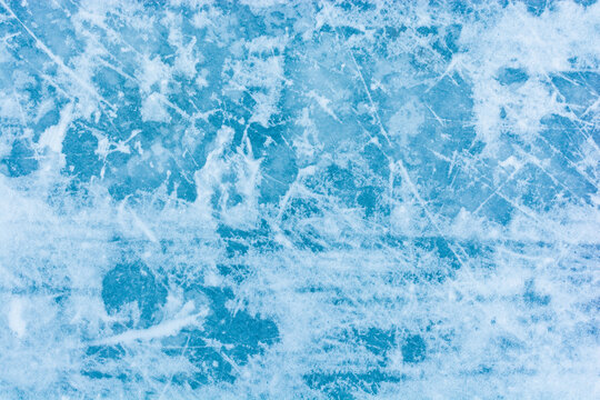 Ice blue background with skate tracks. Skating rink. Frozen water, sea. Frosty ice texture with scratches in winter.