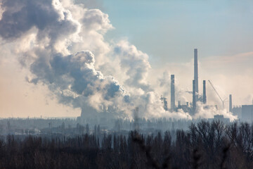 Smoke from chimneys at the plant in the rays of the sunset as a background.