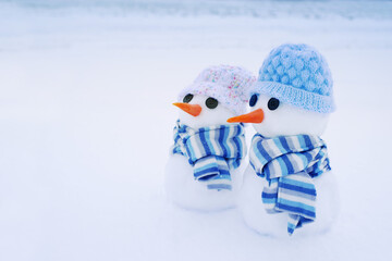 Two little cute snowmen in hats and scarves on the snow on a winter day, close-up. Holiday card...