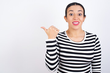 Lovely young beautiful woman wearing stripped t-shirt against white background pointing aside with forefinger, showing at copy space having news about bargains