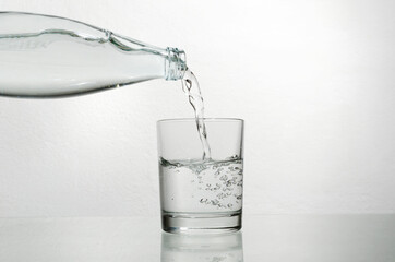 Closeup of glass bottle and glass full of fresh water.Pouring cold water from glass bottle into the glass cup against bright background