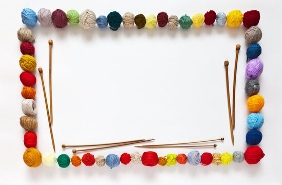 Decorative frame made of balls of colorful woolen yarn and wooden knitting needles for hand knitt on white background. Needlework concept. Place for text and advt. Mock up, flat lay, copy space