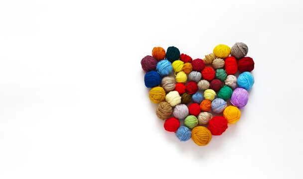 Set of balls of woolen multicolored yarn for hand knitting in the shape of heart on white background. Handmade and DIY concept for St. Valentine's Day. Place for text. Flat lay, mock up, copy space