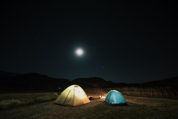 Camping in the mountains under the moon. A tent pitched up and glowing under the sky.