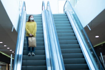 lone woman in a protective mask standing on the escalator steps