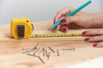 Young woman working in carpentry, marking measurements on a wooden strip with a pencil