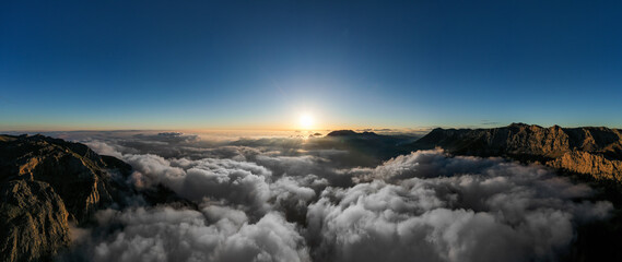 Beautiful scenic mountain landscape with morning mountains, cloudy blue sky and light of rising sun at the hazy horizon.