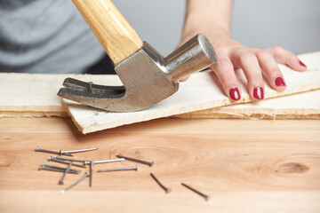 A young woman removing a nail from a piece of wood using a claw hammer - obrazy, fototapety, plakaty