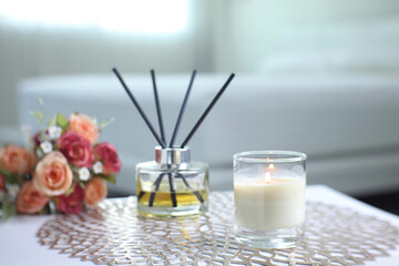 glass of aroma scented candle is on the white table with bouquet of rose and reed diffuser glass bottle in the white bedroom with background of light from the window in the morning of valentine day