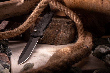 Knife at an angle on the background of stones and rope. Knife on granite and marble stone. The...