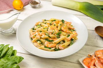 Pasta with shrimps, leeks and spinach in a white plate with ingredients on a white rustic table. Close-up. 