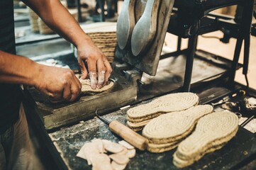 Manos trabajando en fábrica. Suelas de calzado de yute. Industria.
