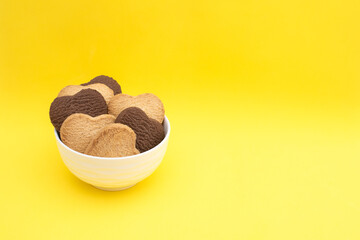 Miscellaneous cookies in a white plate on a yellow background close up