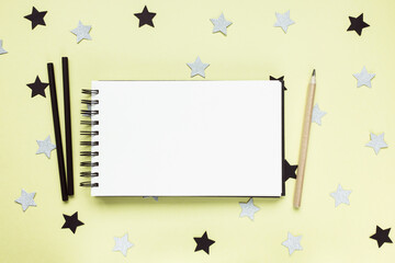 Open sketchbook or notebook, charcoal and wooden pencils on artist desk workspace, yellow with black and silver stars background. Creative concept, empty page, mock up. Flat lay, top view, copy space
