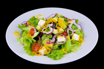 Salad with avocado and feta cheese - avocado, cucumber, feta, bell pepper, cherry tomatoes, lettuce. Closeup on a white plate on black background