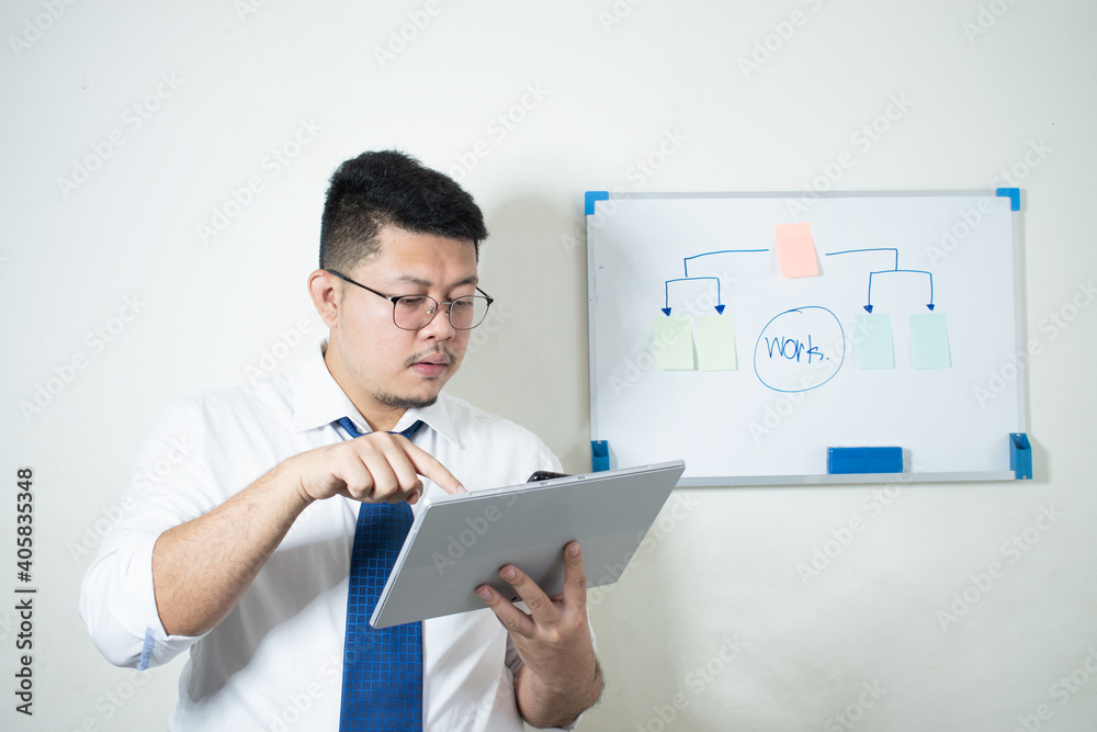 Wall mural young asian businessman wear a white shirt tie a blue tie using his tablet