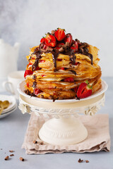 Crepes pancake cake with custard cream, chocolate topping and berries strawberries on vintage stand.