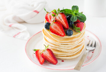 Stack of homemade little pancakes with honey, fresh strawberries and sauce on light wooden background. Selective focus.