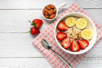Oatmeal Porridge with Strawberries, Almonds and Banana in white bowl. Healthy Breakfast with Oatmeal and Fresh Organic Strawberry. vegan food. healthy food concept