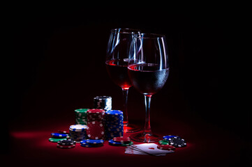 Casino. Poker. Game chips lie next to glasses of red wine on a table against a red background. Game...