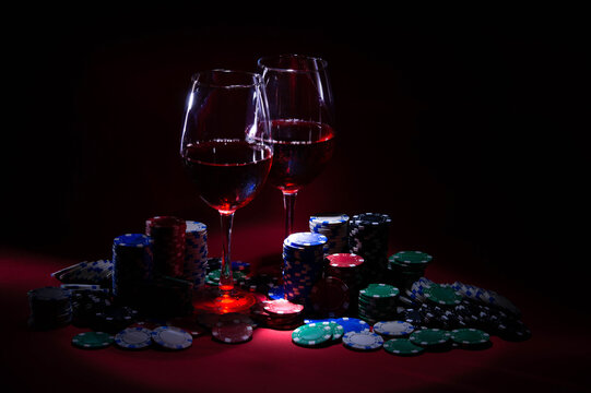 Casino. Poker. Game chips lie next to glasses of red wine on a table against a red background. Game chips for betting in gambling. Poker chips.
