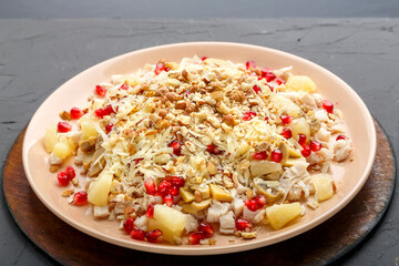 A plate with salad with chicken, pineapple, pomegranate and nuts on a concrete background on a wooden stand close-up.