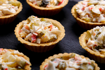 Tartlets with salad on a black wooden board laid out in a circle close-up.