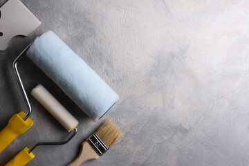Spatulas for application of putty and brushes and rollers for painting on a gray concrete background.Top view