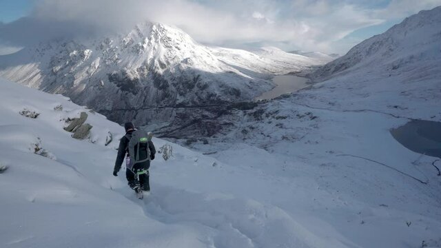 A man walking cautiously and dangerously down a snow covered mountain trail