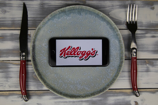 Viersen, Germany - May 9. 2020: Closeup of mobile phone on plate and wood table, cutlery with logo lettering of kelloggs food company (focus on center)