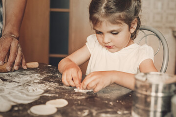 Fototapeta na wymiar girl 3 years old sitting at the table in kitchen and sculpts from dough
