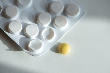 Yellow tablet pill, white plastic blister, natural light and shadows