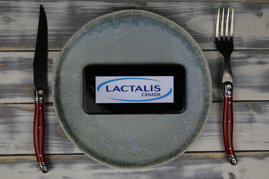 Viersen, Germany - May 9. 2020: Closeup of mobile phone on plate and wood table, cutlery with logo lettering of french lactalis food company (focus on center)