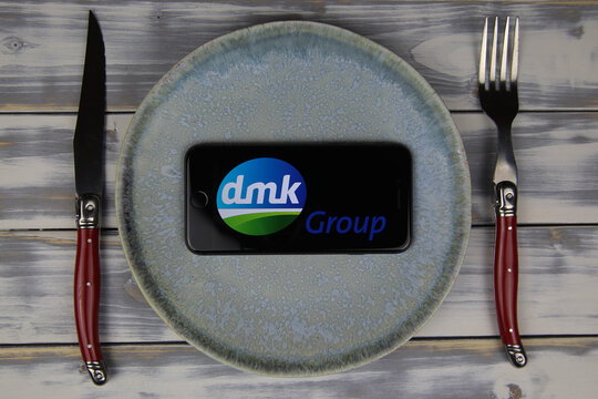 Viersen, Germany - May 9. 2020: Closeup of mobile phone on plate and wood table, cutlery with logo lettering of deutsches Milchkontor dmk dairy prodcuts company (focus on center)
