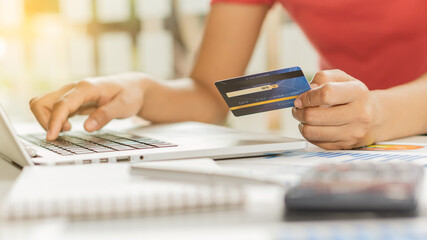 A young business woman holding a blue credit card in hand and using a laptop computer to shop online and dial the number on the credit card.